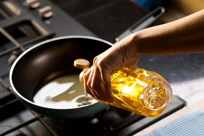 olive oil being put into a frying pan by a chef.