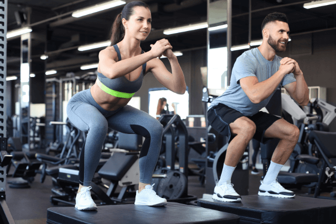 woman and man doing squats in the gym on a black box