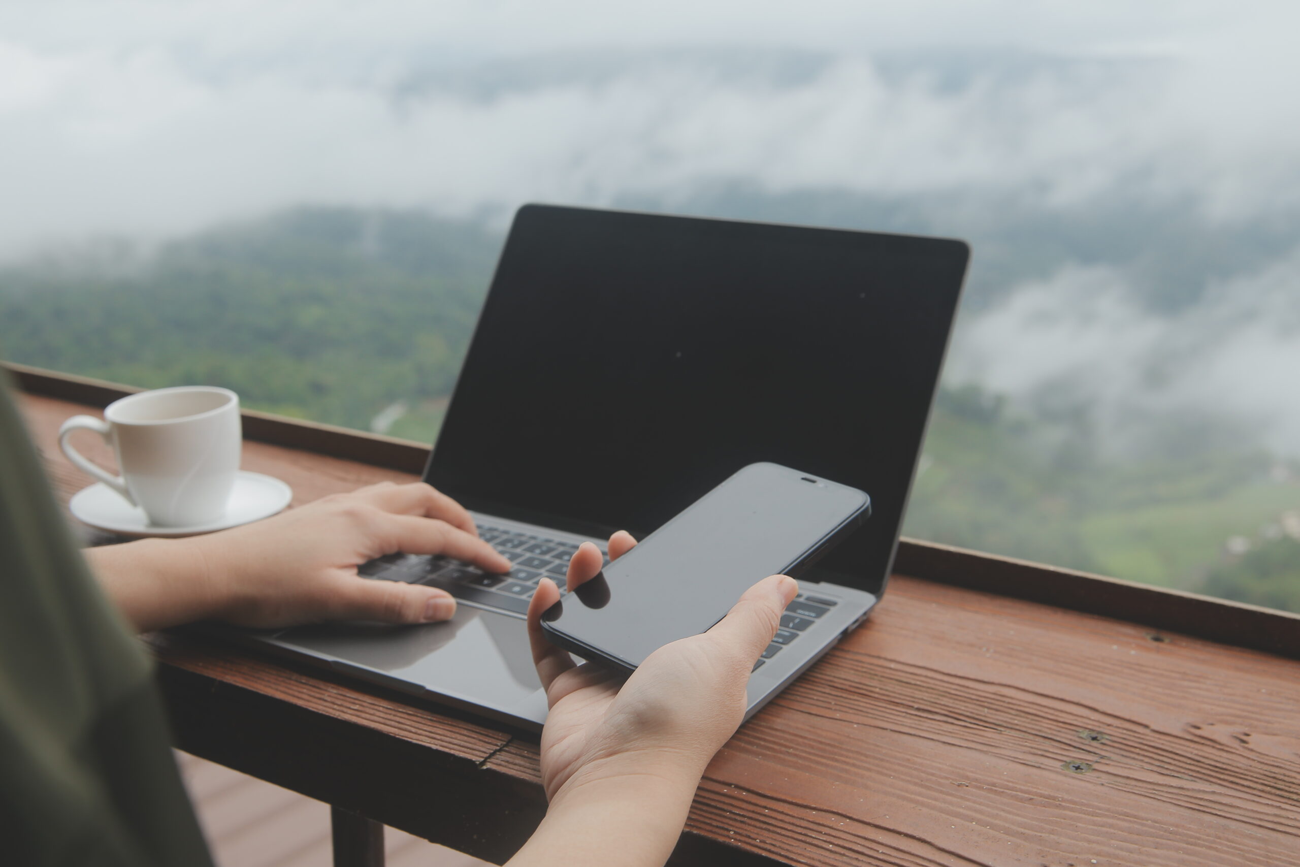Young man freelancer traveler wearing hat anywhere working online using laptop and enjoying mountains view