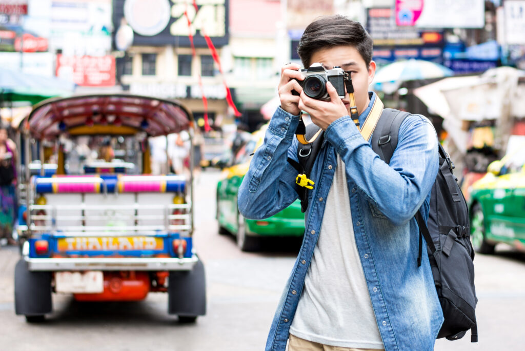 Young Asian man independent tourist photographer taking photo while traveling in Khao san road, Bangkok, Thailand on holidays